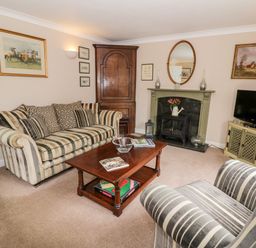 A living room with striped sofa and armchair wooden coffee table fireplace and television at Rosemead in Moreton-In-Marsh
