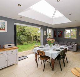 A dining area with a table and chairs next to a gray sofa and an open door to a garden at Rosemead in Moreton-In-Marsh