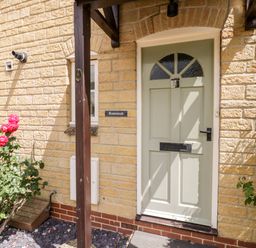A front door with a porch and pink roses by the side of a stone house at Rosemead in Moreton-In-Marsh