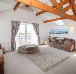 A living room with two sofas a large round ottoman and wooden beams at Bay View in Trearddur Bay