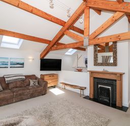 A living room with wooden beams a brown sofa a flat screen tv a wooden fireplace and a decorative sailboat at Bay View in Trearddur Bay
