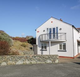 A two-story white house with a small balcony and stone wall outside at Bay View in Trearddur Bay