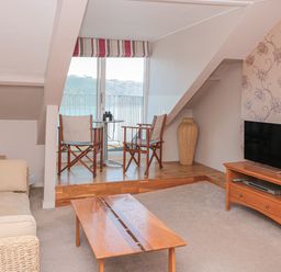 A living room with sofa table chairs tv and sliding glass door overlooking water at Manor Studio in Dartmouth