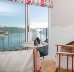 A small seating area with two chairs and a round table with binoculars by a glass door overlooking a river at Manor Studio in Dartmouth