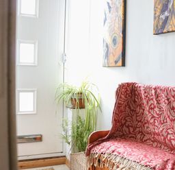 A hallway with a wooden bench covered with a patterned red blanket two paintings on a white wall and green plants near a white door with square windows at 21 Florence Road in Pakefield
