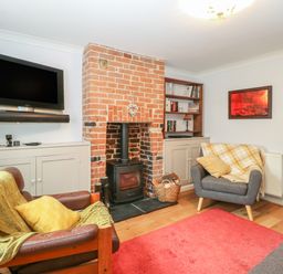 A living room with a brick fireplace wood stove a mounted television two armchairs and a red rug at 21 Florence Road in Pakefield