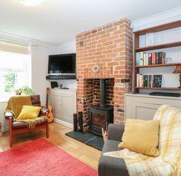 A living room with a brick fireplace wooden shelves with books a gray sofa with yellow cushions and a brown armchair with a yellow throw at 21 Florence Road in Pakefield