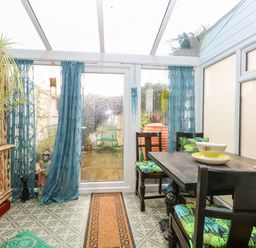 A conservatory with a wooden table and chairs with patterned cushions and an ornate cabinet at 21 Florence Road in Pakefield