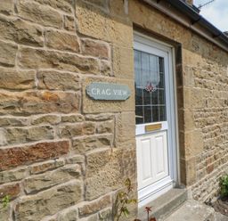 A stone house exterior with a white door and a plaque reading Crag View in West Woodburn