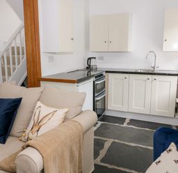 A kitchen with white cabinets a stove and a beige sofa with cushions at Pine Cottage in Sedbergh