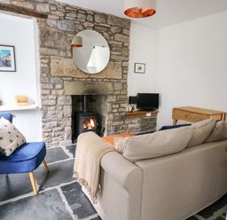 A living room with a stone fireplace a beige sofa a blue chair and a small tv at Pine Cottage in Sedbergh