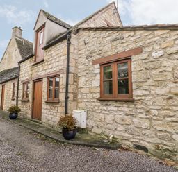 The exterior of a stone cottage with wooden windows and doors and potted plants on a gravel driveway at Chapel Cottage in Leonard Stanley near King's Stanley