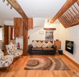 A living room with a leather sofa floral armchairs wooden beams and a wall-mounted fireplace at Chapel Cottage in Leonard Stanley near Kings Stanley