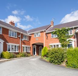 A row of red brick houses with white windows and doors surrounded by bushes and greenery at Sea View Cottage in Menai Bridge
