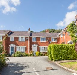 A driveway leading to red brick townhouses with white doors and windows surrounded by green hedges at Sea View Cottage in Menai Bridge