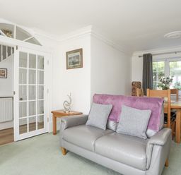 A living room with a grey leather sofa and purple throw next to a wooden dining table and chairs at Sea View Cottage in Menai Bridge