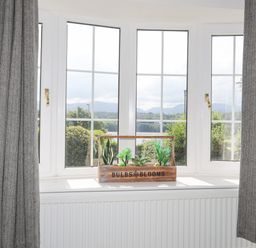 A window with white frames and gray curtains with a wooden planter box holding small plants on the windowsill at Sea View Cottage in Menai Bridge