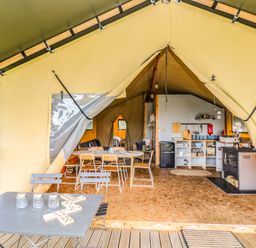 An open tent with a kitchen area dining table wooden chairs and an outdoor table with jars and a domino game at Honey @ Stars & Embers Glamping in Grampound