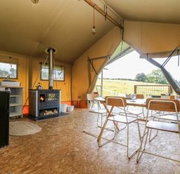 An interior view of a tent with a wood stove dining table with chairs and a small kitchen area at Honey @ Stars & Embers Glamping Grampound
