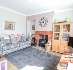 A living room with a patterned sofa a wood burning stove a wooden cabinet and a television at Lillies Pad in Methwold near Feltwell