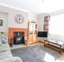 A living room with a floral sofa a brick fireplace a wall clock a TV on a wooden stand and patterned curtains at Lillies Pad Methwold near Feltwell
