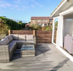 An outdoor patio with a wicker sectional sofa and a glass top table at Caban Tywod in Abersoch