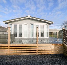 A raised wooden deck with glass railings and a white building with double doors at Caban Tywod in Abersoch