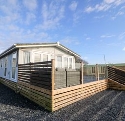 A small house with a wooden deck and glass fence under a blue sky at Caban Tywod in Abersoch