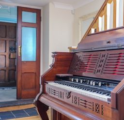 A wooden antique piano in a hallway near a door with frosted glass panels at Capel Hermon in Llanynghenedl near Bodedern