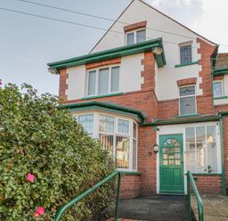 The exterior of a brick and white house with green framed windows a green door and a bush with pink flowers at Hillcrest in Scarborough