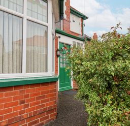 A front entrance with a green door and green framed window beside a brick wall and large leafy bushes at Hillcrest Scarborough