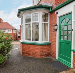 Front entrance of a red brick house with a green door and bay window with curtains and a bush with flowers near the pathway at Hillcrest in Scarborough