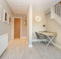 A hallway with a wooden door three framed pictures a radiator a desk a chair a clock and stairs at Bishop Fell in Newby Bridge