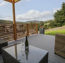 An outdoor patio with wicker furniture and a glass table with a wine bottle and glasses at Bishop Fell in Newby Bridge