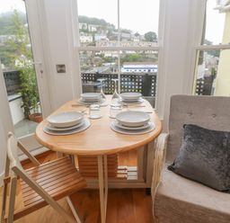 A dining table set for four with plates and glasses next to a window and two chairs at 1 River View in Looe