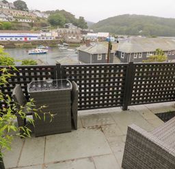 A balcony with a wicker table and chairs overlooking a river with boats and buildings at 1 River View in Looe