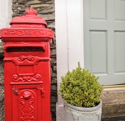 A red postbox next to a door and a potted plant at The Postmasters House in Windermere