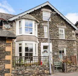 Stone house with bay windows white door and small garden fenced by a stone wall at The Postmasters House in Windermere