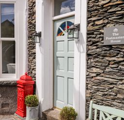Front entrance with light green door red mailbox stone wall and two potted plants at The Postmasters House in Windermere