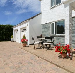 An outdoor patio area with a table and four chairs and flower pots near a white house with a double garage at Trevore Farmhouse in Chacewater
