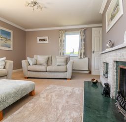 A living room with beige sofas a light blue ottoman and a fireplace at Trevore Farmhouse in Chacewater