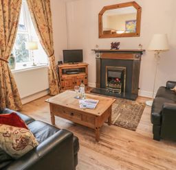 A living room with two leather sofas a wooden coffee table a fireplace and floral curtains at Manod View in Blaenau Ffestiniog