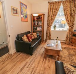 A living room with leather sofas, a wooden coffee table, bookshelf, TV stand, patterned curtains, and framed paintings at Manod View in Blaenau Ffestiniog