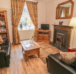 A living room with black leather sofas a wooden coffee table a fireplace and bookshelves at Manod View in Blaenau Ffestiniog