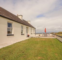 A grass yard with a patio table and chairs with a red umbrella outside a single story house at Newtown East near Kilkee County Clare