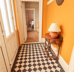 A hallway with checkered floor tiles an orange wall a small wooden table with a lamp and a view into a bedroom at Newtown East near Kilkee County Clare