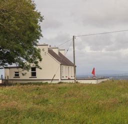 A white house with a rooftop patio and red umbrella surrounded by grass and a large tree at Newtown East near Kilkee County Clare