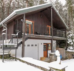 A snow-covered chalet with a balcony and stairs in a forested area at Torbreck Chalet in Kincraig