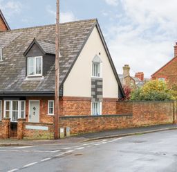 A brick and stucco house with a tiled roof on a street corner with a brick wall and greenery at Little Wash Cottage in Hunstanton