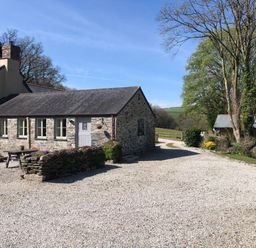 Stone cottage with a gravel driveway and trees surrounding a garden at Mimis Cottage in St Neot